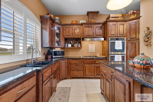 kitchen featuring appliances with stainless steel finishes, light tile patterned floors, dark stone counters, and sink