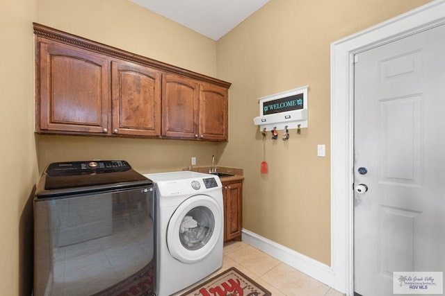 clothes washing area with washing machine and dryer, sink, light tile patterned flooring, and cabinets