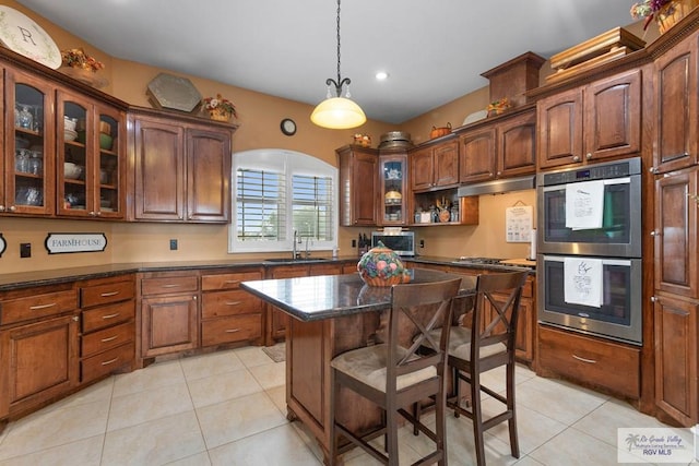 kitchen featuring stainless steel appliances, dark stone countertops, a kitchen island, and light tile patterned flooring