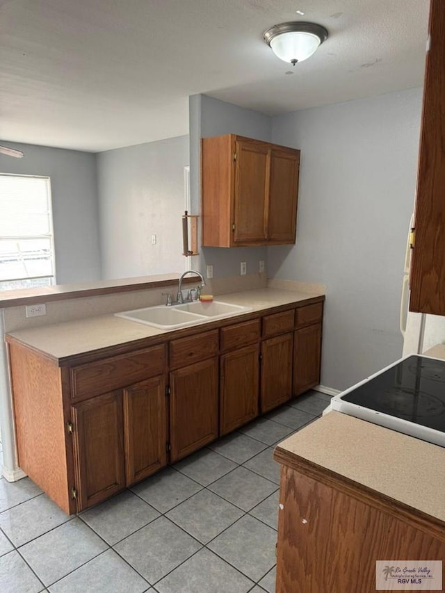kitchen featuring a sink, a peninsula, brown cabinets, and light countertops