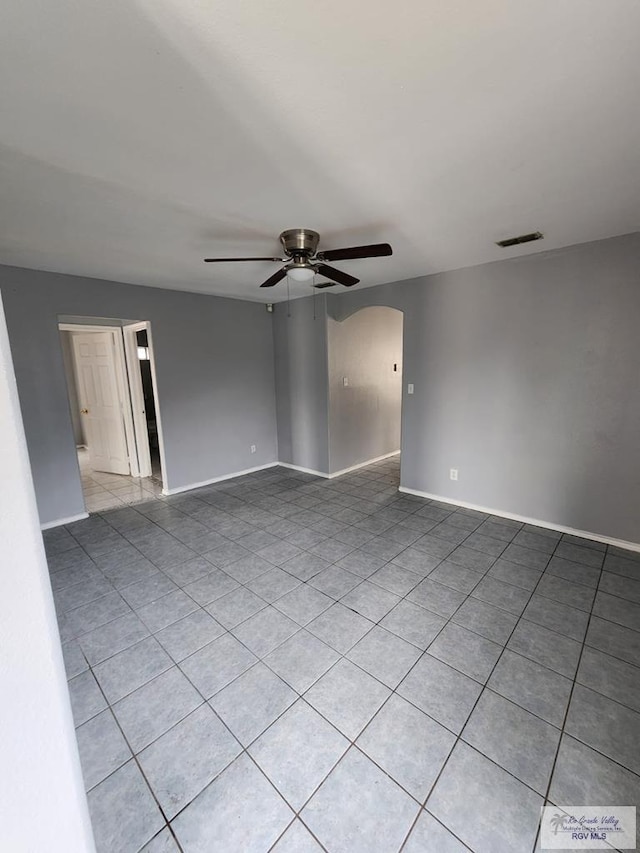 unfurnished room with ceiling fan, visible vents, arched walkways, light tile patterned floors, and baseboards
