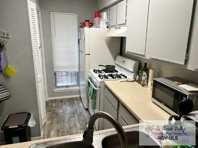 1900 E Elizabeth St Unit F13, Brownsville, TX 78520 - kitchen featuring black microwave, white gas range, under cabinet range hood, white cabinetry, and wood finished floors