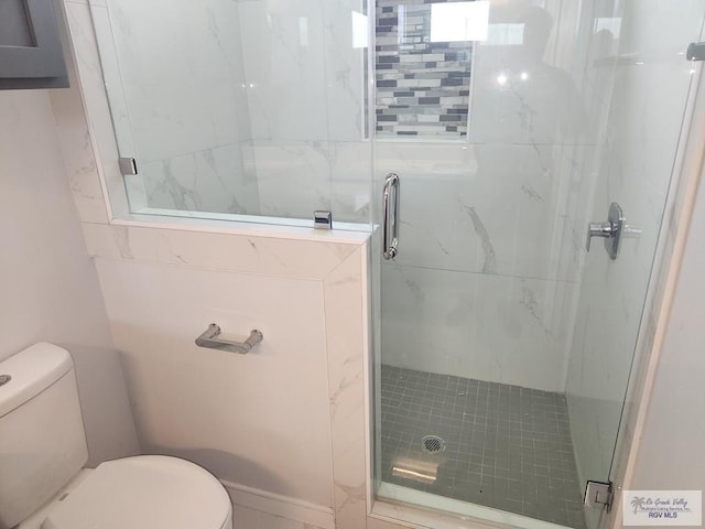 bathroom featuring a shower with shower door and toilet