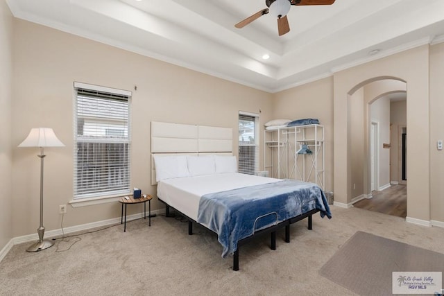 carpeted bedroom featuring multiple windows, a raised ceiling, ceiling fan, and ornamental molding