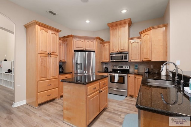 kitchen with sink, stainless steel appliances, dark stone counters, light hardwood / wood-style floors, and a kitchen island