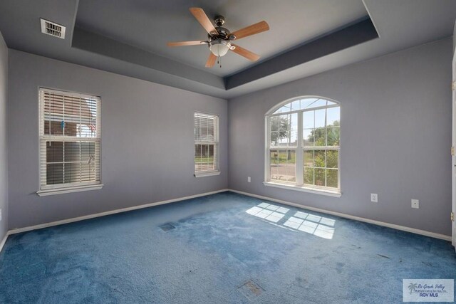 empty room featuring carpet flooring, a tray ceiling, visible vents, and baseboards