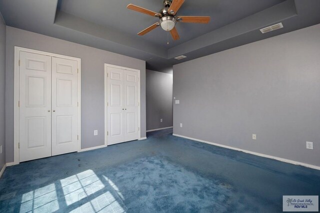 unfurnished bedroom with visible vents, multiple closets, baseboards, a tray ceiling, and carpet flooring