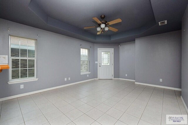 tiled empty room with a raised ceiling, baseboards, a ceiling fan, and visible vents