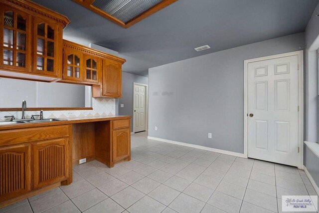 kitchen featuring visible vents, light tile patterned floors, brown cabinets, and glass insert cabinets