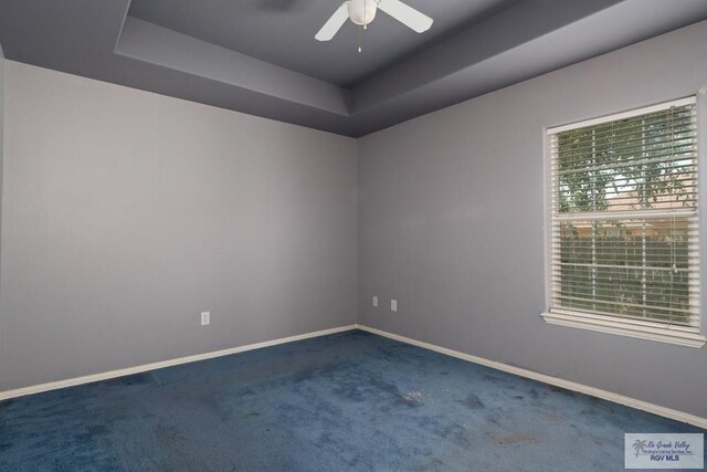 carpeted empty room with a ceiling fan, a tray ceiling, and baseboards