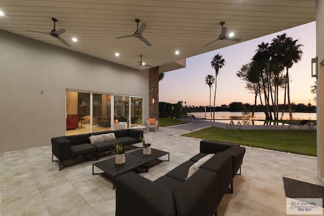 patio terrace at dusk with a lawn, outdoor lounge area, ceiling fan, and a water view