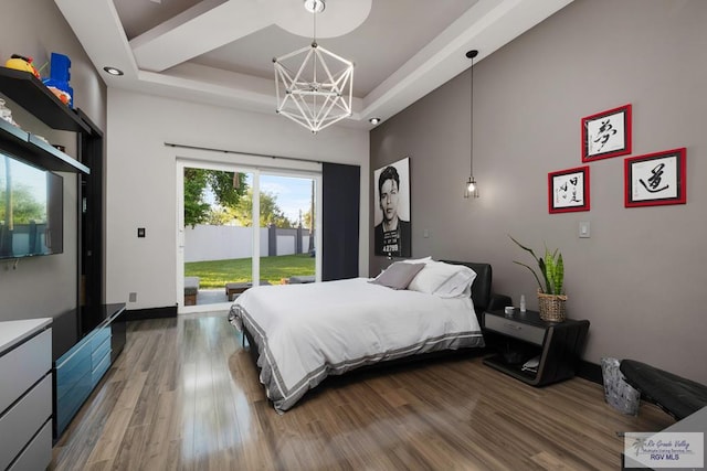 bedroom with access to outside, a raised ceiling, hardwood / wood-style floors, and a chandelier