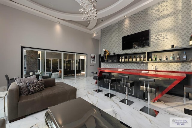 bar with a tray ceiling, a high ceiling, and an inviting chandelier