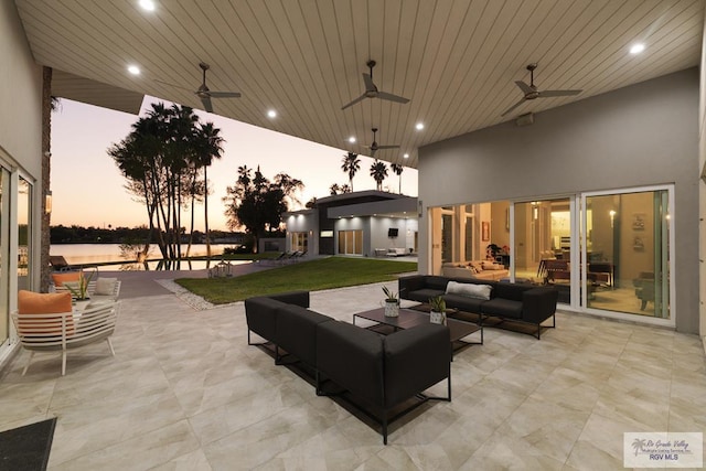 patio terrace at dusk with an outdoor living space, a water view, ceiling fan, and a lawn