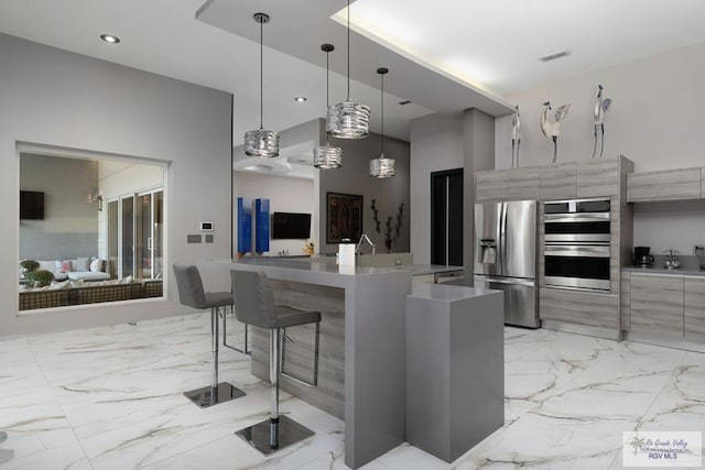 kitchen with a breakfast bar, hanging light fixtures, stainless steel appliances, and a center island with sink