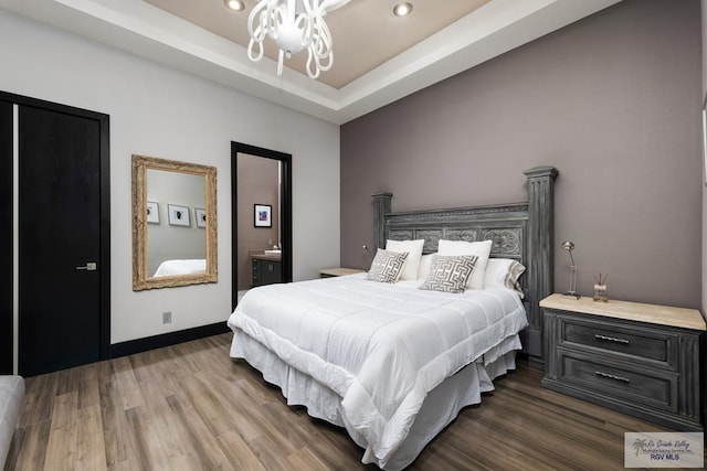 bedroom featuring a raised ceiling, dark hardwood / wood-style flooring, and connected bathroom