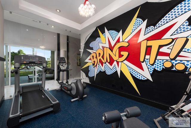 exercise room with a raised ceiling and a chandelier