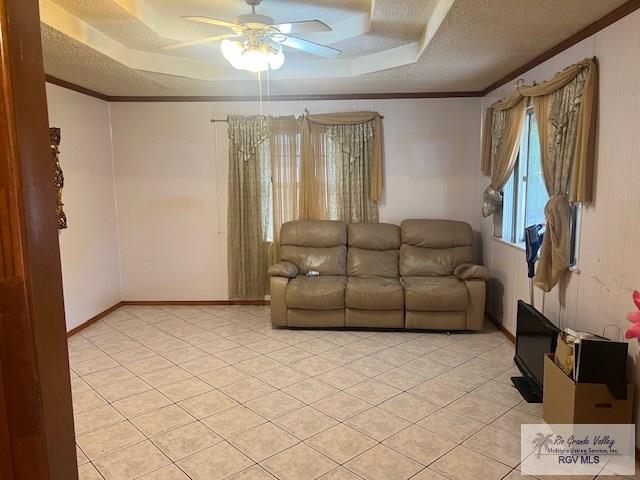 living room with a raised ceiling, ceiling fan, and ornamental molding