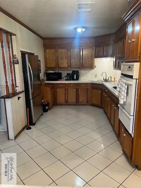 kitchen featuring white oven, sink, stainless steel fridge, ornamental molding, and a textured ceiling