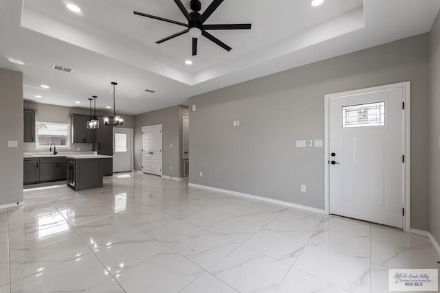 unfurnished living room featuring sink, a tray ceiling, and ceiling fan with notable chandelier