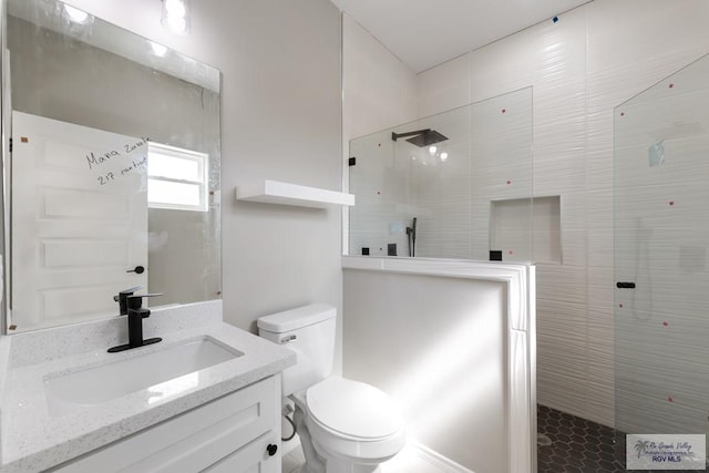 bathroom with vanity, toilet, and a tile shower