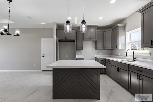 kitchen featuring hanging light fixtures, a center island, sink, and gray cabinetry