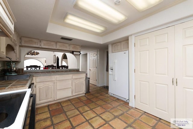 kitchen featuring tile countertops, white fridge with ice dispenser, light brown cabinetry, and range