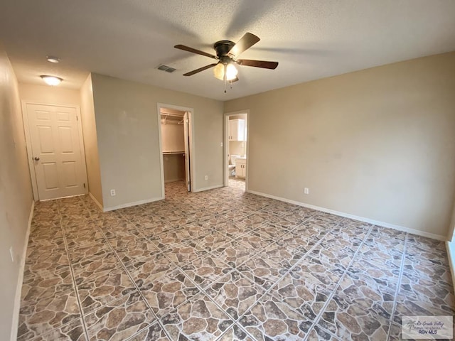 unfurnished bedroom featuring a textured ceiling, a closet, a spacious closet, and ceiling fan