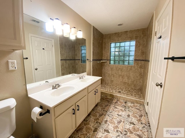 bathroom featuring a tile shower, vanity, a textured ceiling, and toilet