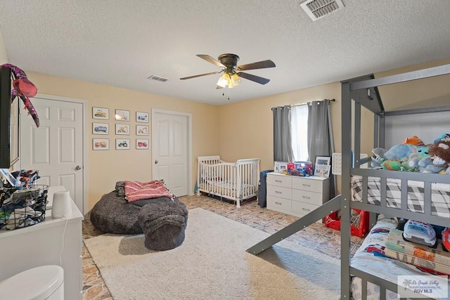 bedroom with a textured ceiling, light colored carpet, and ceiling fan