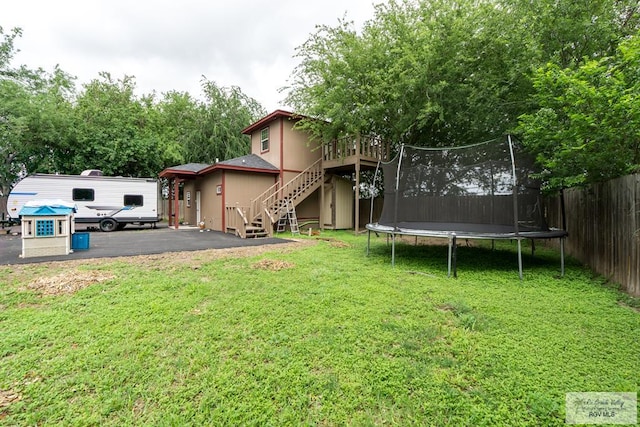 view of yard with a trampoline, fence, a wooden deck, and stairway