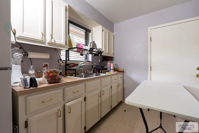 kitchen featuring white cabinetry, light countertops, freestanding refrigerator, and a sink