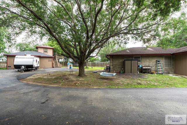 view of yard featuring stairs, aphalt driveway, and fence