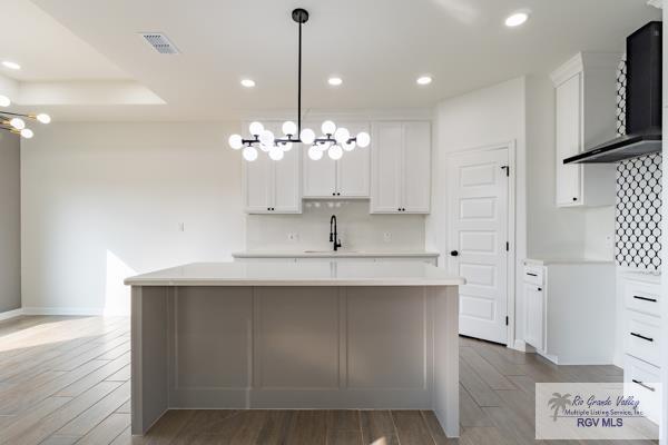 kitchen with hardwood / wood-style flooring, white cabinetry, hanging light fixtures, backsplash, and an island with sink