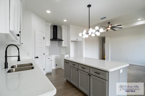 kitchen with pendant lighting, sink, dark hardwood / wood-style flooring, a center island, and wall chimney range hood