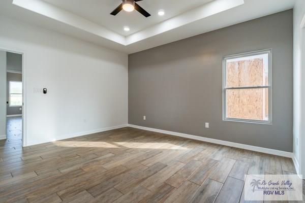 empty room with light hardwood / wood-style flooring, a raised ceiling, and ceiling fan