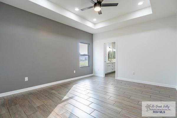 unfurnished room with light hardwood / wood-style flooring, ceiling fan, and a tray ceiling