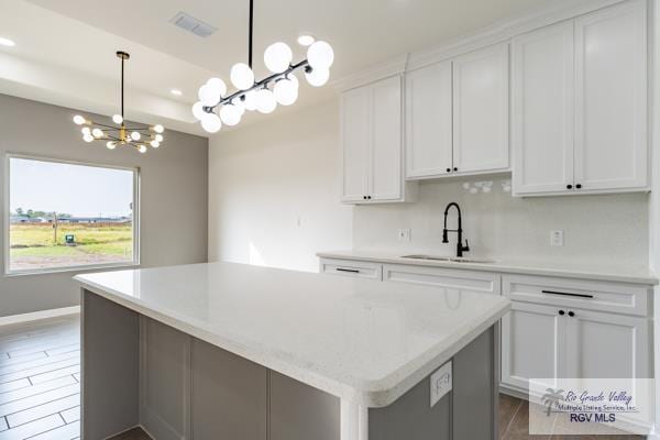 kitchen with sink, dark wood-type flooring, white cabinetry, a kitchen island, and decorative light fixtures