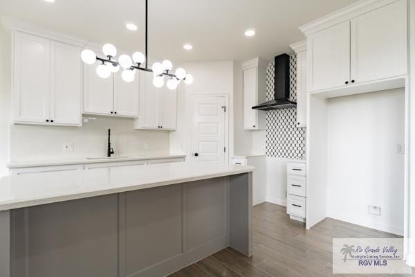 kitchen with wall chimney range hood, white cabinetry, hanging light fixtures, tasteful backsplash, and dark hardwood / wood-style flooring