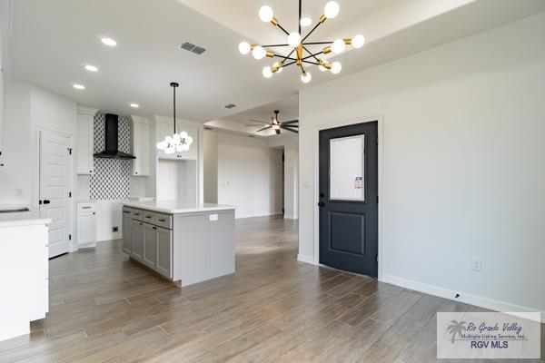 kitchen featuring hardwood / wood-style flooring, a kitchen island, decorative light fixtures, and wall chimney exhaust hood