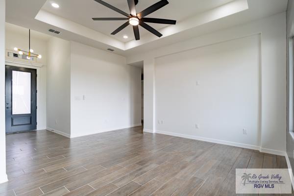 unfurnished room with a raised ceiling, ceiling fan with notable chandelier, and hardwood / wood-style floors