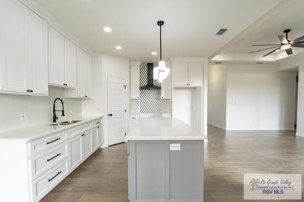 kitchen featuring sink, white cabinetry, a center island, decorative light fixtures, and wall chimney exhaust hood