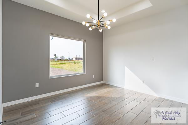 empty room featuring a chandelier, wood-type flooring, and a raised ceiling