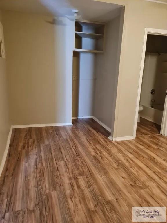 unfurnished bedroom featuring baseboards, ensuite bathroom, wood finished floors, and a closet