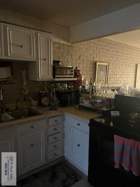 401 Boca Chica Blvd Unit 110, Brownsville, TX 78520 - kitchen featuring a sink, white cabinetry, light countertops, brick wall, and decorative backsplash