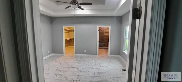 unfurnished bedroom featuring ceiling fan, a raised ceiling, a spacious closet, and a closet