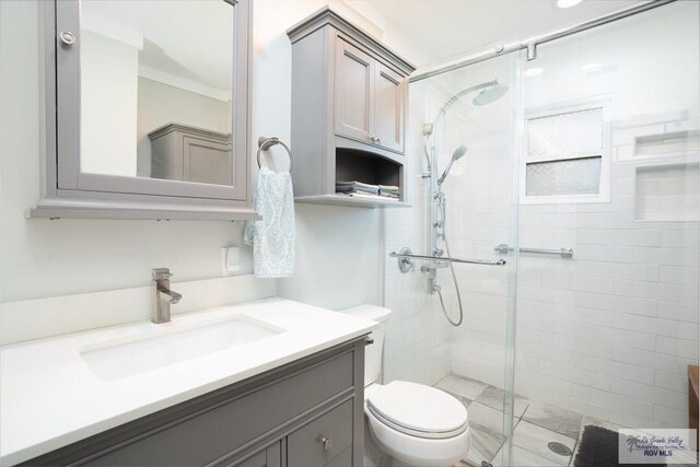 bathroom featuring vanity, toilet, a shower with door, and ornamental molding