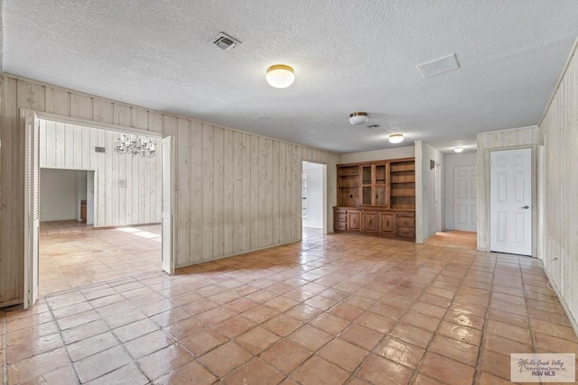 spare room with a textured ceiling, visible vents, and wood walls