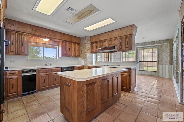 kitchen with brown cabinets, light countertops, wallpapered walls, a kitchen island, and visible vents