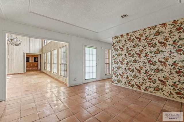 unfurnished room featuring baseboards, wallpapered walls, a textured ceiling, and visible vents
